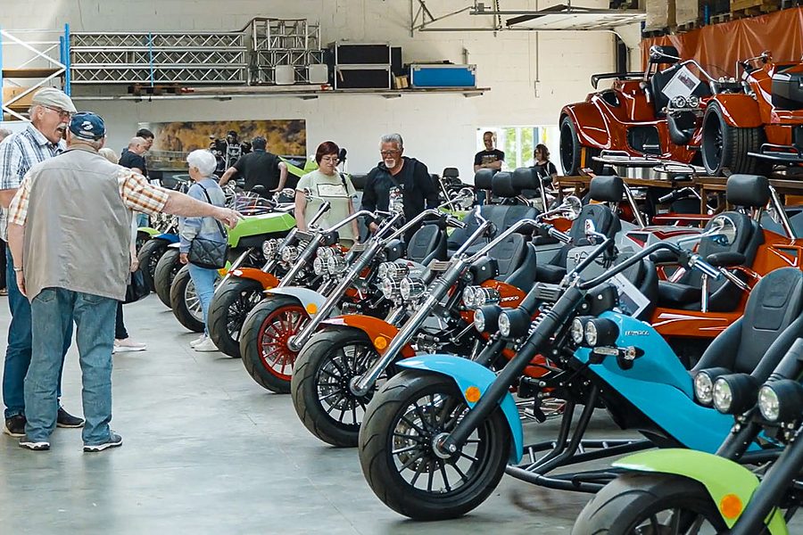 Besucher der Hausmesse zwischen einer langen Reihe bunter rewaco Trikes in der Halle
